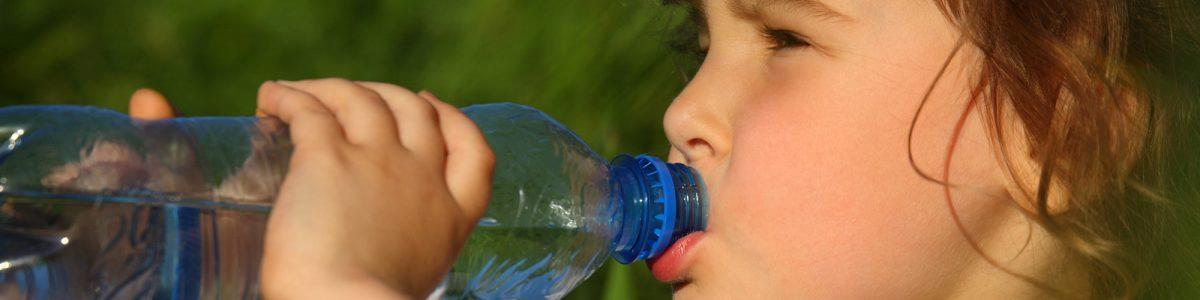 Et nærbillede af et lille barn der drikker vand af en vandflaske. Barnet holder med begge hænder rundt om flasken.