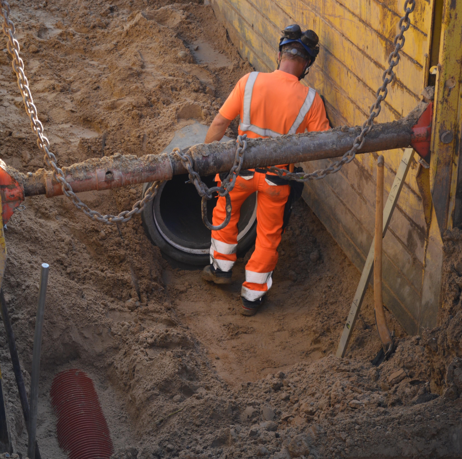 På billedet ser man en mand i orange arbejdstøj. Han står nede i et hul fyldt med sand. I hullet ligger der et stort cementrør.