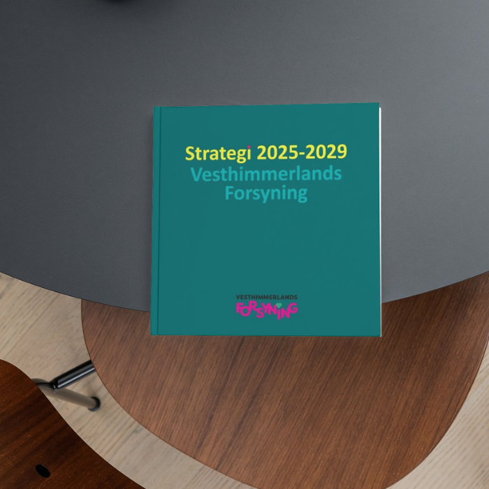 Strategi 2025-2029 En folder der ligger på en bordplade. Folderen beskriver Vesthimmerlands Forsynings strategi for 2025-2029.