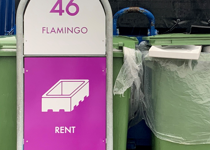 Et skilt med teksten flamingo. Ved siden af skiltet ser man nogle grønne affaldscontainere, hvor der stikker et stykke flamingo op.
