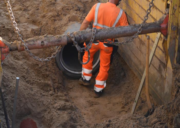 Udgravning til kloakrør. Mand i orange arbejdstøj står foran hullet til et kloakrør. 