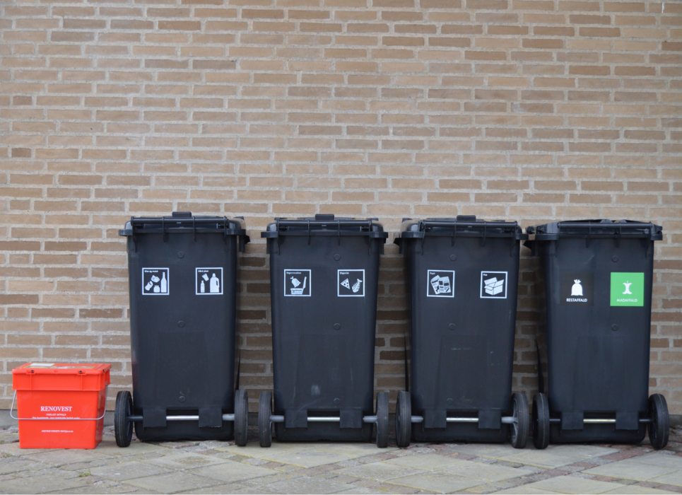 Fire sorte affaldsbeholdere på stribe og en rød miljøkasse