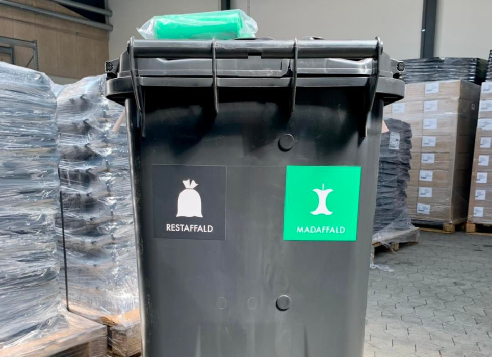 Sort affaldsbeholder med grønne poser på låget og labels på kroppen